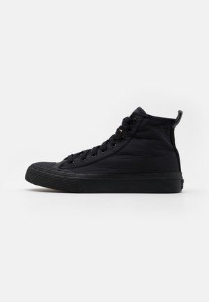 Basket montante noire avec embout en caoutchouc texturé, laçage à l’avant et languette sur fond blanc uni.