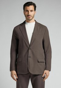 Brauner Leinenblazer mit Schalkragen, zwei Knöpfen und seitlichen Taschen. Kombiniert mit einem hellen, Rundhals-Pullover. Glatte Textur.