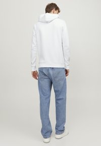 Hvit hettegenser med snor, avslappet passform, kombinert med lyseblå baggy jeans og hvite sneakers. Ingen merkbare mønstre eller detaljer.