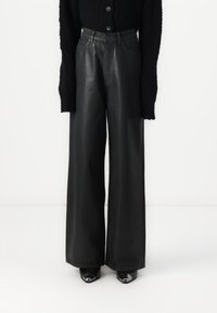 Pantalon en cuir noir à jambes larges, texture lisse, taille haute, et design classique à cinq poches. Associé à un pull en maille texturée noir.