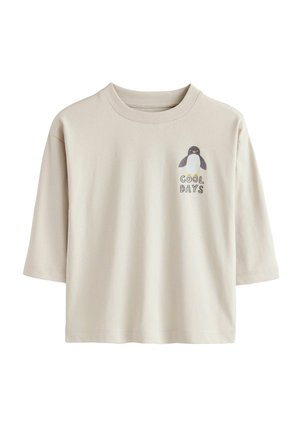 Lühikeste varrukatega beež T-särk, mis on valmistatud puuvillast, ja millel on vasakus rinnakus pingviini graafiline kujundus ning tekst "JAHEPÄEVAD".