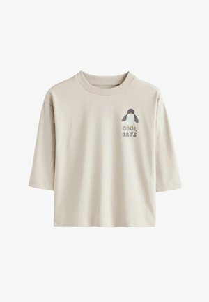 Lühikeste varrukatega beež T-särk, mis on valmistatud puuvillast, ja millel on vasakus rinnakus pingviini graafiline kujundus ning tekst "JAHEPÄEVAD".