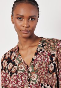 Blusa con estampado floral en tonos oscuros, con escote en V y detalles de botones. Presenta una mezcla de flores burdeos, verdes y crema sobre una tela suave.