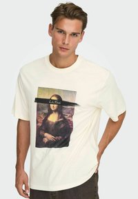Hvid bomulds t-shirt med grafik af Mona Lisa, delvist skjult af en sort penselstrøg og teksten "L. da Vinci." Kortærmet.