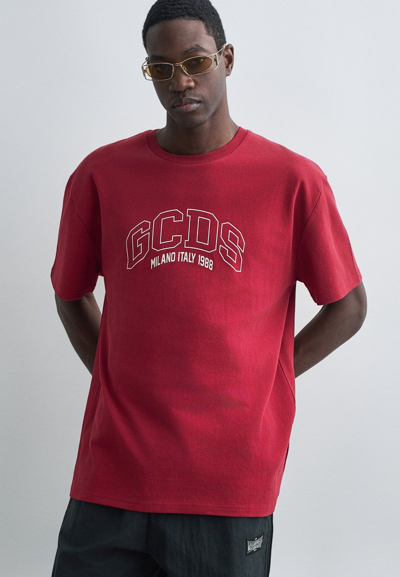 Crvena pamučna majica s bijelim natpisom "GCDS MILANO ITALY 1988", kratkih rukava i opuštenog kroja. Mekana tekstura, jednostavan dizajn s okruglim izrezom.