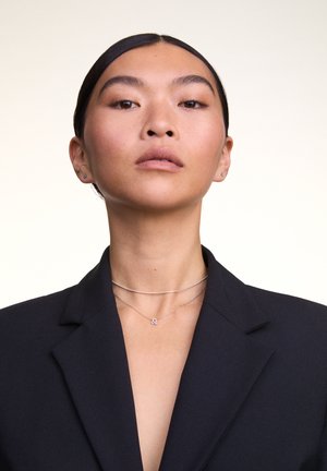 Collares de plata en capas sobre una persona que lleva un blazer negro. Un collar incluye un pequeño charm; se puede apreciar la textura suave de la tela.