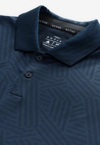 Marineblå poloshirt med et struktureret mønster, tre-knaps placket og en klassisk krave. Etiket viser "NEXT ACTIVE" branding.