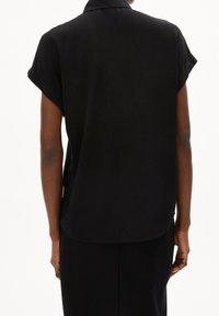 Blusa nera a maniche corte con colletto, caratterizzata da una vestibilità ampia, una texture liscia e un orlo arrotondato. Il capo è abbinato a una gonna nera coordinata.
