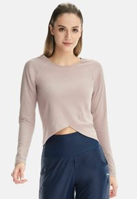 Light pink long-sleeve top with a wrap design, featuring smooth fabric and a rounded neckline, paired with dark blue athletic pants.