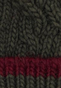 Tessuto lavorato a maglia verde scuro con una prominente striscia orizzontale rossa. Il filato è spesso, con un motivo a trecce in rilievo.