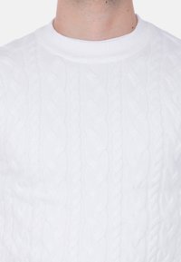 Maglione bianco a costine con scollatura rotonda e motivo testurizzato con trecce in rilievo. Tessuto liscio e morbido con una silhouette aderente.