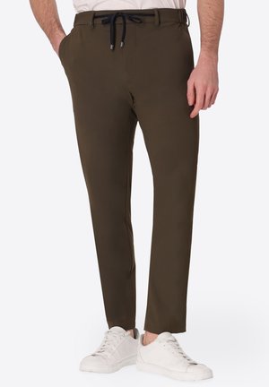 Uomo che indossa pantaloni slim fit verde oliva con coulisse nera, sneakers bianche e camicia bianca infilata.