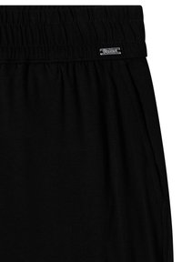 Pantalon noir avec taille élastique, poche latérale et petite étiquette de marque métallique rectangulaire cousue près du haut.