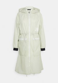 Veste longue à capuche beige clair avec fermeture éclair devant, taille et ourlet réglables, deux poches avant zippées et poignets intérieurs noirs.