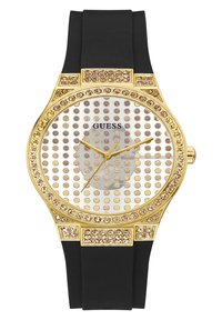 Reloj de tono dorado con esfera redonda, adornos de cristal transparente, correa de goma negra y manecillas doradas sobre un fondo de puntos.