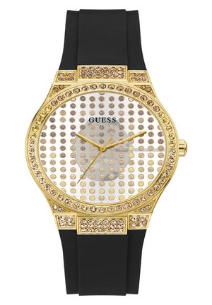 Montre dorée avec un cadran rond, embellissements en cristal clair, bracelet en caoutchouc noir et aiguilles dorées sur un fond à pois.