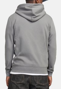 Grå hoodie med en stor hætte bagpå, ribbede manchetter og kant, blød stoftekstur og et enkelt design. Bæres med mørke jeans.