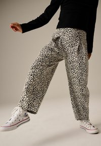Pantalones holgados hechos de una tela ligera con un patrón de manchas en blanco y negro, combinados con unas zapatillas de lona blancas.