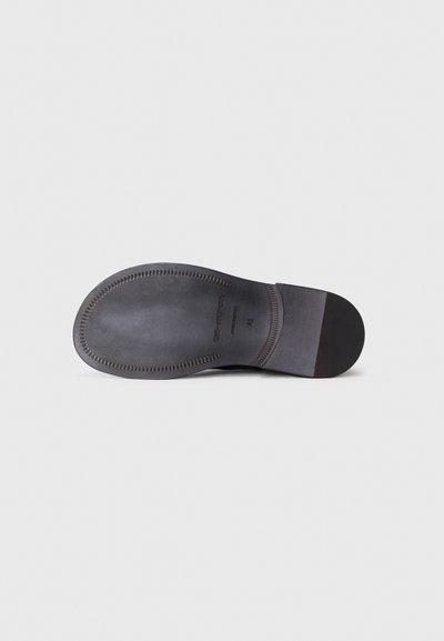 Suela de zapato de cuero negro con un acabado liso, con punta redondeada, costuras visibles y tacón plano. Diseño limpio, detalles mínimos.