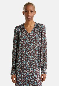 Camicia floreale marrone con maniche lunghe e scollatura a V, caratterizzata da fiori blu e crema, texture morbida e dettagli arricciati alle spalle.