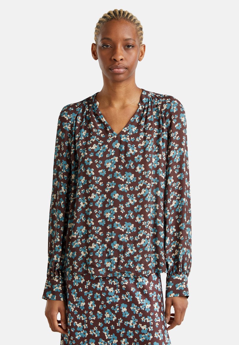 Camicia floreale marrone con maniche lunghe e scollatura a V, caratterizzata da fiori blu e crema, texture morbida e dettagli arricciati alle spalle.