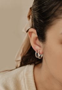 Silberne Creolen, gestapeltes Design mit strukturierten und polierten Abschnitten, die an einem gestochenen Ohr befestigt sind. Neutraler Hintergrund mit sanfter Beleuchtung.