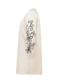 Crème-kleurig langärmige shirt met zwarte bloemenborduursel op één mouw, zachte stof, ronde halslijn, zijsplitten aan de zoom.