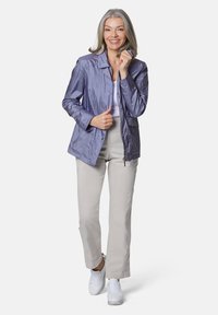 Helle lila, leichte Jacke mit Kragen und Reißverschlusstaschen, kombiniert mit beigen Hosen und weißen Turnschuhen. Glatte Textur, lässiges Design.