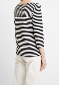 Camicia a maniche lunghe a righe con righe orizzontali blu scuro e bianche, texture a costine sulle spalle, scollo rotondo e vestibilità comoda.