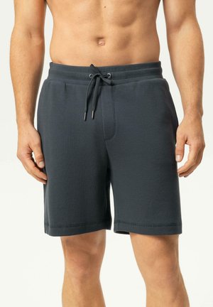 Mann trägt dunkelgraue, strukturierte Shorts mit Kordelzug, gezeigt vom Taillen- bis zum Kniebereich, steht vor einem schlichten hellen Hintergrund.