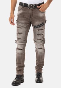 Gräuliche, distressed Jean mit Rissen, schmaler Passform und einem schwarzen Logopatch. Kombiniert mit schwarzen Schnürstiefeln und einem detaillierten Gürtel.