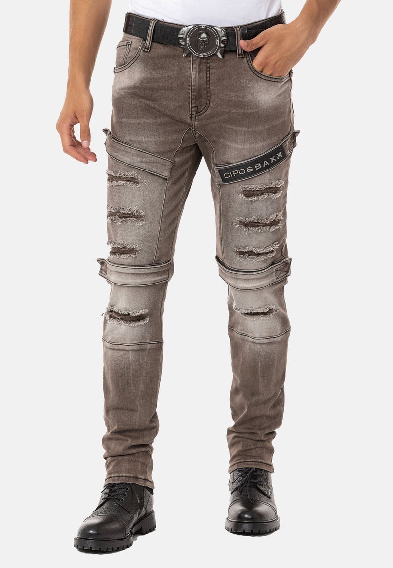 Gräuliche, distressed Jean mit Rissen, schmaler Passform und einem schwarzen Logopatch. Kombiniert mit schwarzen Schnürstiefeln und einem detaillierten Gürtel.
