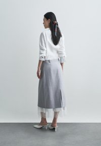 Balta marškinių viršutinė dalis su sukeltomis rankovėmis ir pilka sijoną su nėriniu apdaila bei šonine plyšiu. Modelis dėvi baltus aukštakulnius mules ir raštuotą plaukų kaspiną.