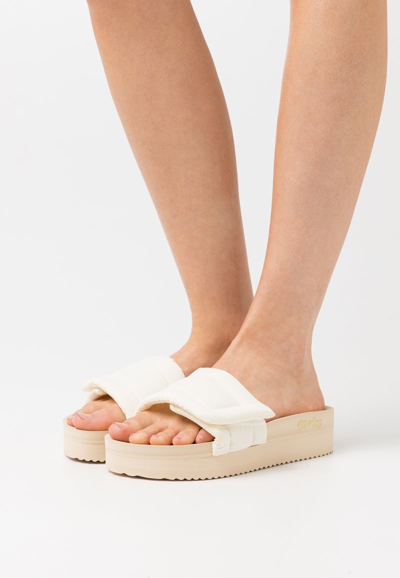 White padded slide sandals with a thick beige platform sole, featuring two strap sections across the foot and textured detailing.