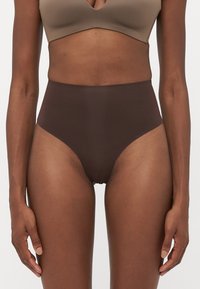 Female torso wearing a brown high-waisted seamless brief and a beige bra against a plain white background.