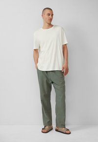 T-shirt en coton blanc à manches courtes associé à un pantalon vert ample et des sandales marron à semelles foncées avec une touche de lanière.