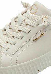 Sneaker in pelle crema con lacci testurizzati, branding sottile in oro e suola bianca rigata. Finitura liscia e design minimalista.