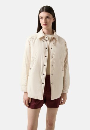 Beige Steppjacke mit durchgehender Knopfleiste, spitzem Kragen und seitlichen Taschen. Verfügt über braune Knöpfe und eine glatte, glänzende Textur.