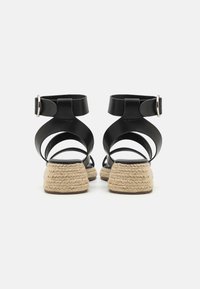 Mustad naha sandaalid ristkülikukujuliste rihmadega, kinnituv pahkluu lukk ja 3,5 cm palmik jute kontsad. Sile tekstuur minimalistliku kujundusega.