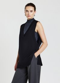 Top nero senza maniche con scollatura a V profonda, realizzato in tessuto testurizzato. Abbinato a pantaloni grigi a gamba larga, dotati di tasche laterali.