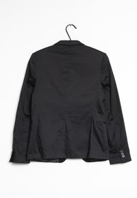 Blazer noir ajusté accroché à un crochet. Présente un col cranté, des poignets boutonnés et une fente arrière unique avec une texture lisse.