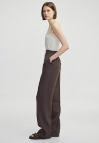 Hnědé kalhoty s širokými nohavicemi, elastickým pasem a bočními kapsami, spárované s přiléhavým, světle béžovým tílkem. Jednoduchý design a lehký materiál.