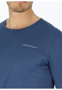 Maglietta sportiva blu con un motivo testurizzato, colletto rotondo e logo visibile. Realizzata in materiale traspirante, adatta per attività all'aperto.
