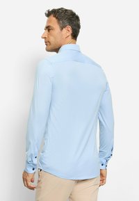 Chemise à manches longues bleu clair en tissu lisse avec un col pointu, des poignets boutonnés et une coupe ajustée.