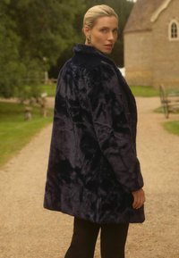 Jūras spēku mākslīgā kažokādas mētelis ar mīkstu, teksturētu virsmu, gariem piedurknēm un plašu apkakli. Mētelim ir brīvs piegriezums, kas sasniedz vidukļa augstumu.