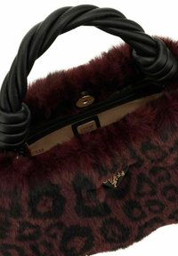 Sac à main en fausse fourrure bordeaux et noire avec motif léopard, poignées en cuir noir torsadées, et logo Guess visible à l'intérieur et à l'extérieur.