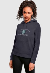 Mørkeblå hættetrøje med "University of Cambridge" tekst og våbenskjold, med kængurulomme og ribbede manchetter. Blødt stof.