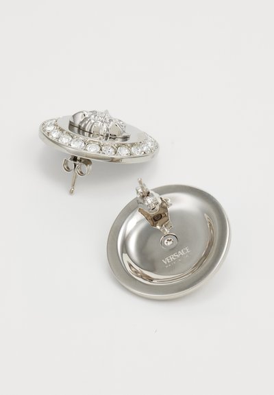 Stříbrné klipové náušnice s vyvýšeným dekorativním prvkem a kruhovým designem ozdobeným čirými krystaly podél okraje.