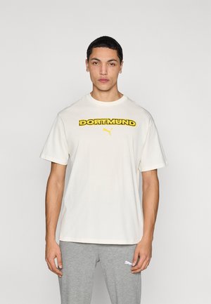 Krém színű rövid ujjú póló "DORTMUND" vastag sárga betűkkel és egy kis Puma logóval. Szürke melegítőnadrággal párosítva.