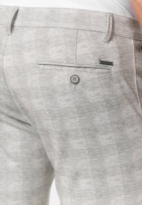 Light grey patterned trousers featuring a subtle check design, a single back pocket with button closure, and a smooth fabric texture.